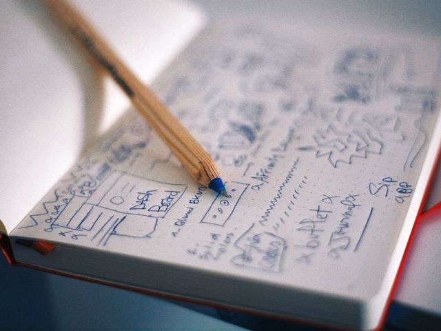 Aufgeschlagenes Notizbuch mit gezeichneten Entwürfen, darauf ein Bleistift