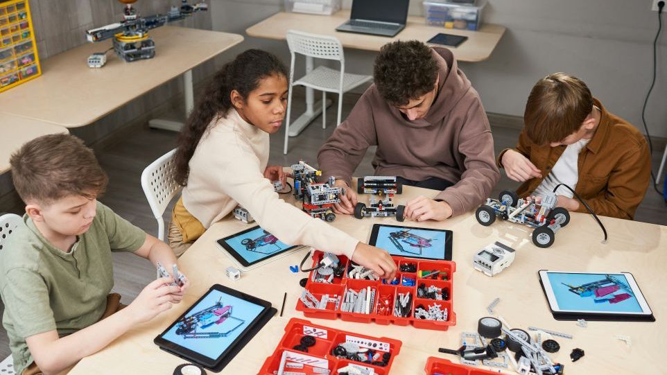 Four children in a classroom are building robots together using digital assembly instructions on tablets
