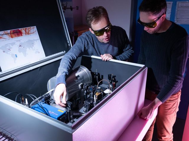 Messtation: Kasten in den Kabel hereinlaufen, technische Komponenten miteinander verknüpft sind und zwei Männer mit schwarzen Brillen, die sich unzerhalten und einen Mechanismus bedienenn