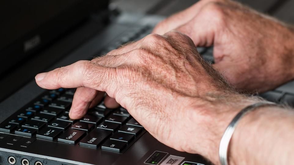 Hands of an elderly person typing on laptop 