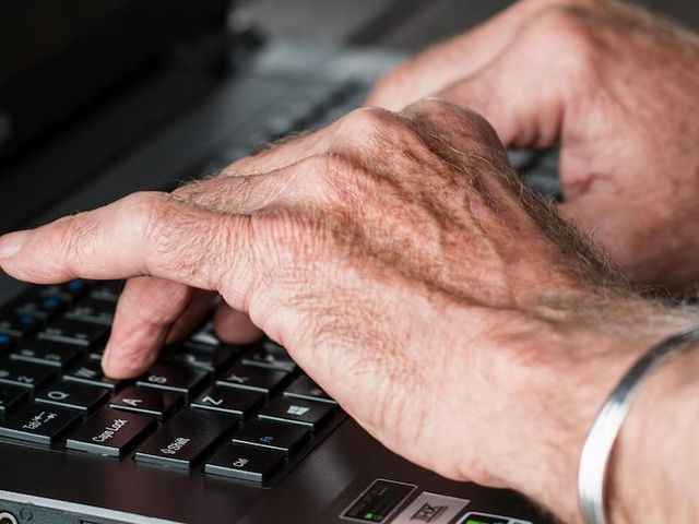 Hände einer älteren Person tippen auf Laptop 