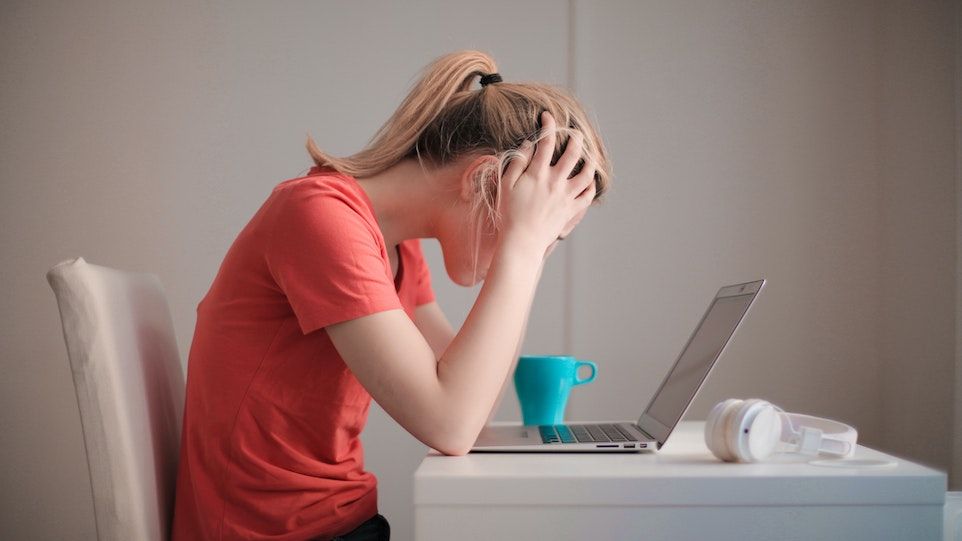 Frau im roten T-Shirt sitzt verzweifelt vor ihrem Laptop