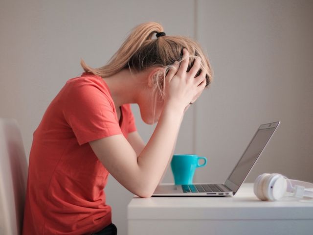 Frau im roten T-Shirt sitzt verzweifelt vor ihrem Laptop