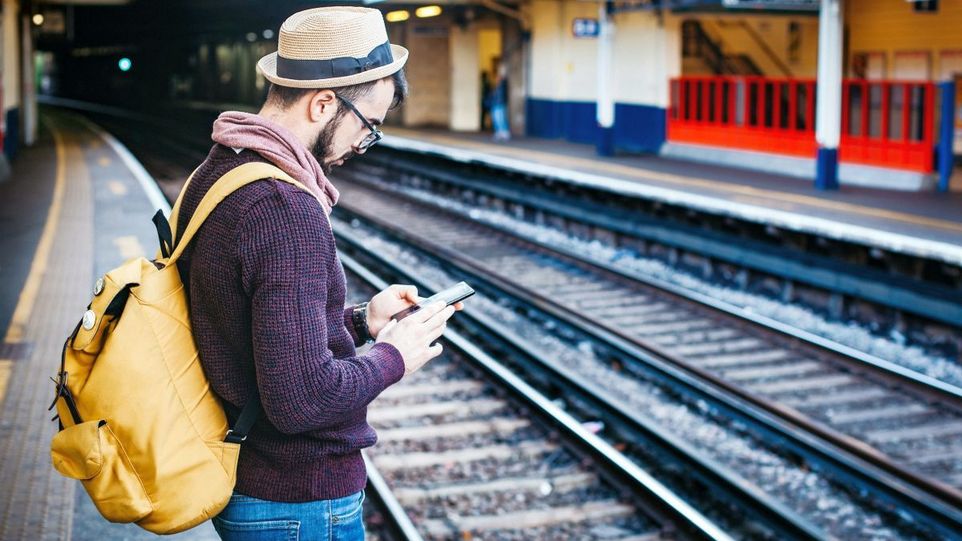 Mann mit Telefon, während er tagsüber vor der Bahnschiene steht