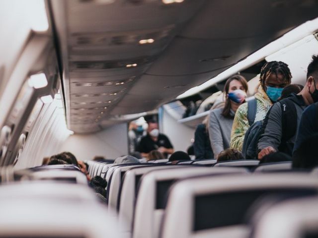 Menschen mit Mund-Nasen-Schutz im Mittelgang eines Flugzeugs