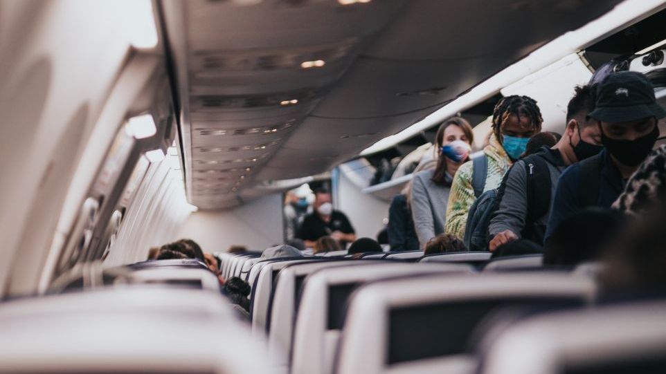 Menschen mit Mund-Nasen-Schutz im Mittelgang eines Flugzeugs
