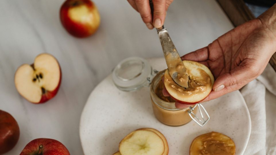 Aufgeschnittene Apfelscheiben werden mit Erdnussbutter bestrichen
