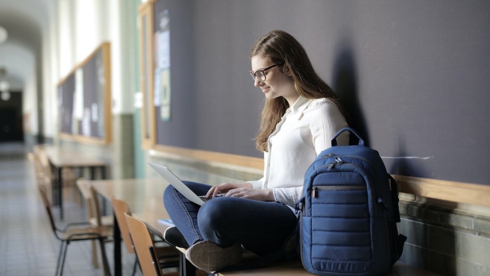 Junge Frau sitzt mit Laptop in Schulflur