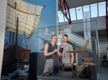 Mann und Frau mit Handy vor Museumsobjekt