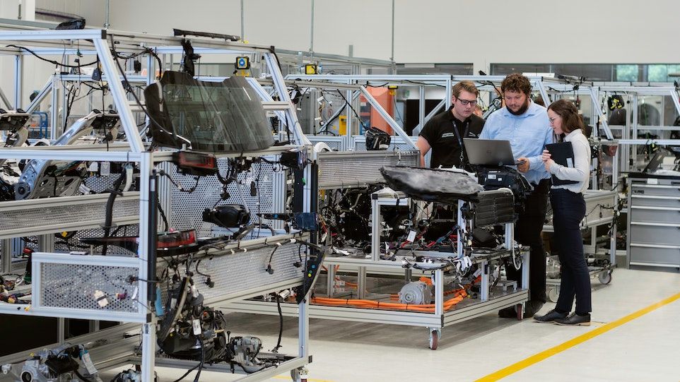 Drei Personen stehen vor einem Laptop in einer Produktionshalle