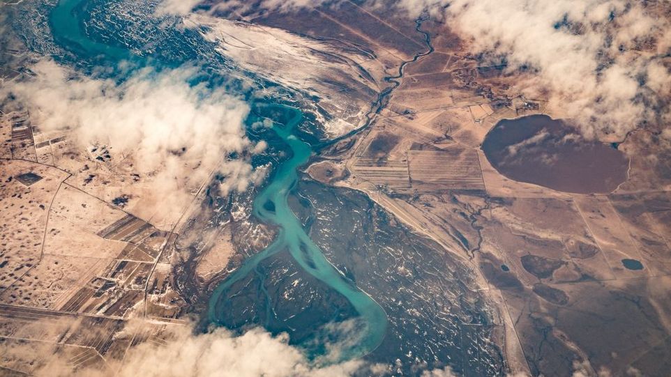 Luftbild einer isländischen Landschaft mit rauchenden Kratern, einem Fluss, Feldern und Siedlungen