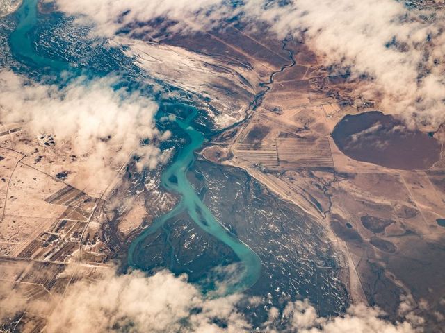 Luftbild einer isländischen Landschaft mit rauchenden Kratern, einem Fluss, Feldern und Siedlungen