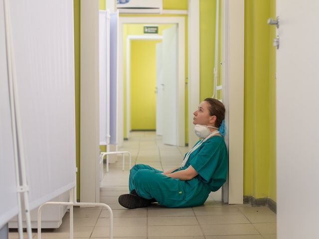 Erschöpfte Krankenhaus-Mitarbeiterin sitzend in einem Flur