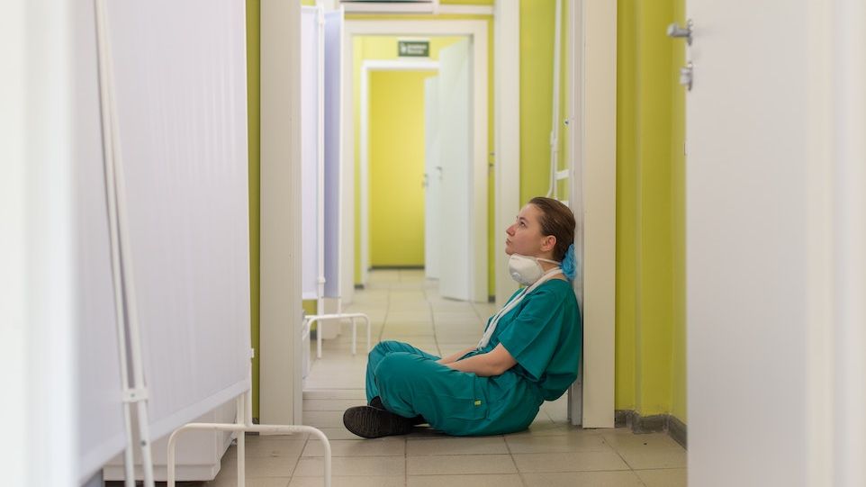 Erschöpfte Krankenhaus-Mitarbeiterin sitzend in einem Flur