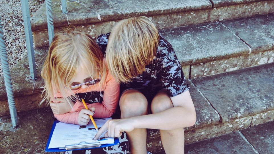 Zwei Kinder beugen sich über ein Aufgabenblatt