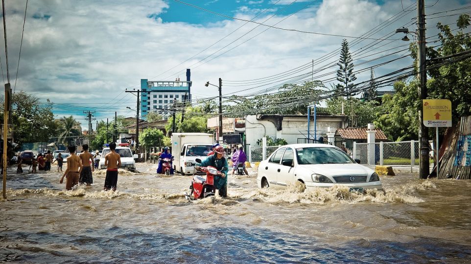 Menschen bewegen sich zu Fuß, mit Autos oder Motorrädern durch eine überflutete Straße