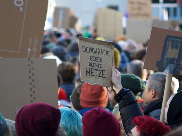 Demonstrierende mit Pappschild: "Demokratie gegen rechte Hetze"