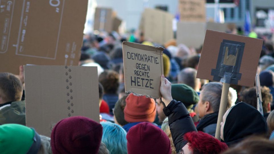 Demonstrierende mit Pappschild: "Demokratie gegen rechte Hetze"
