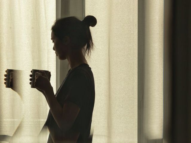 Frau vor mit Tasse vor verhangenem Fenster
