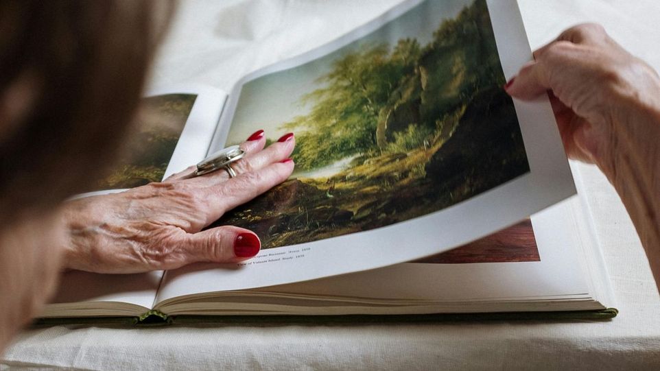 Hand einer alten Dame schlägt einen Kunstband auf