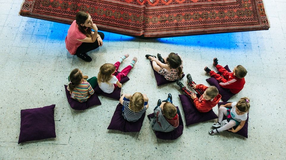 Gruppe von Kindern mit Erzieherin, auf Kissen sitzend