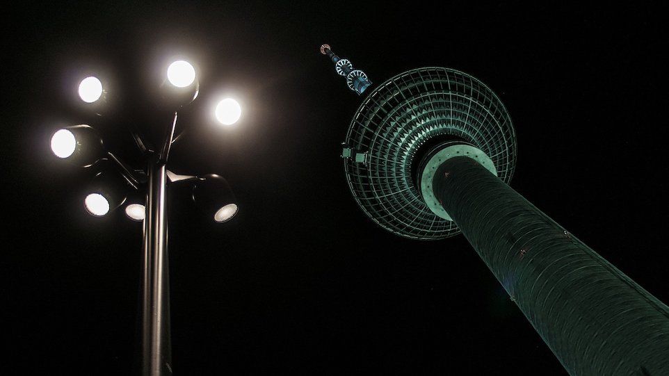 Berliner Fernsehturm bei Nacht, im Vordergrund helle Straßenbeleuchtung