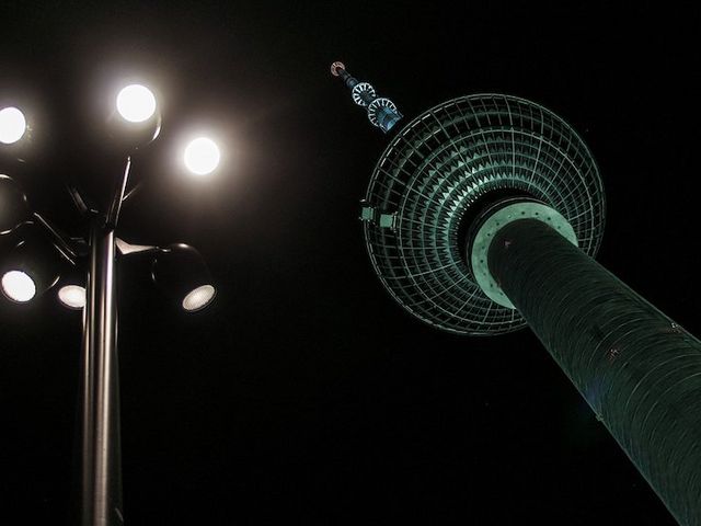 Berliner Fernsehturm bei Nacht, im Vordergrund helle Straßenbeleuchtung