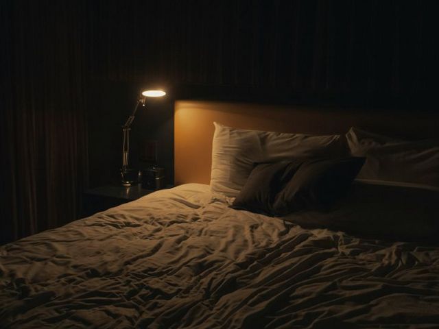 Ungemachtes Bett mit Nachtischlampe bei Nacht