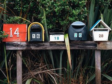 Briefkästen unterschiedlichen Formats und Farbe auf einem Holzzaun