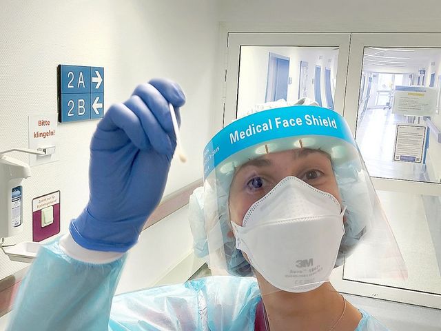Weibliche Pflegekraft mit Medical Face Shield und Maske, die ein Teststäbchen in die Kamera hält. 