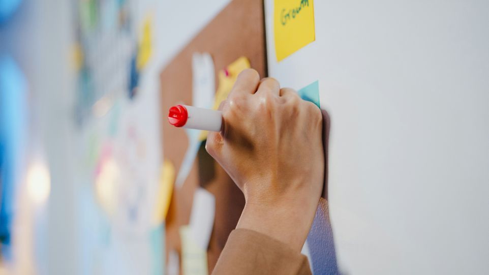Whiteboard mit Post-its und schreibender Hand