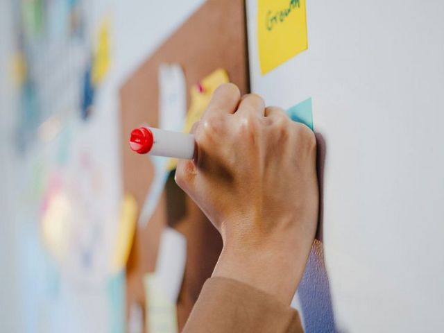 Whiteboard mit Post-its und schreibender Hand
