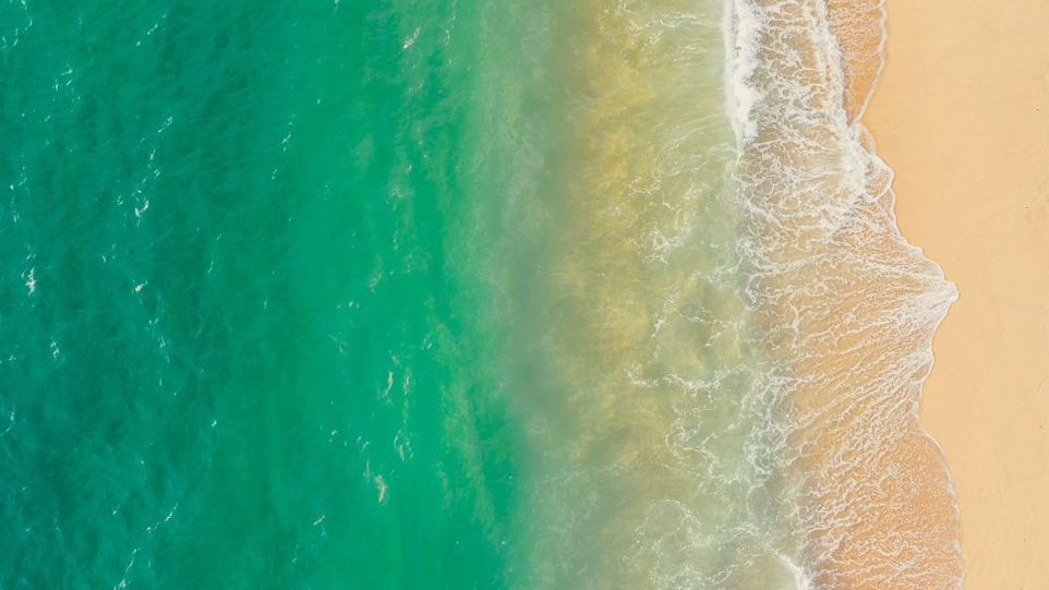Türkisfarbenes Meer, das in sanften Wellen an einen Strand schlägt