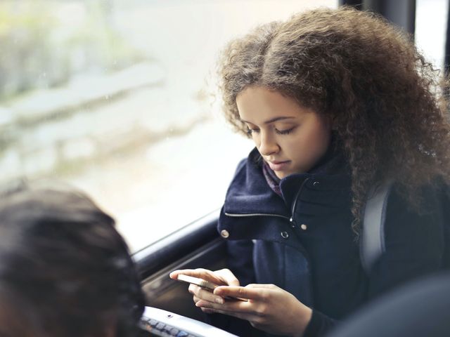 Junge Frau sitzt in öffentlichem Verkehrsmittel mit Blick auf ihr Smartphone. 