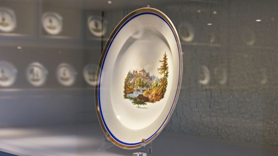 Ein Teller des Herder-Services mit bergbaulichem Motiv in romantischer Tradition. Teller des Herder-Services in einer Vitrine, das Motiv zeigt eine Berglandschaft mit Burg und Fluss