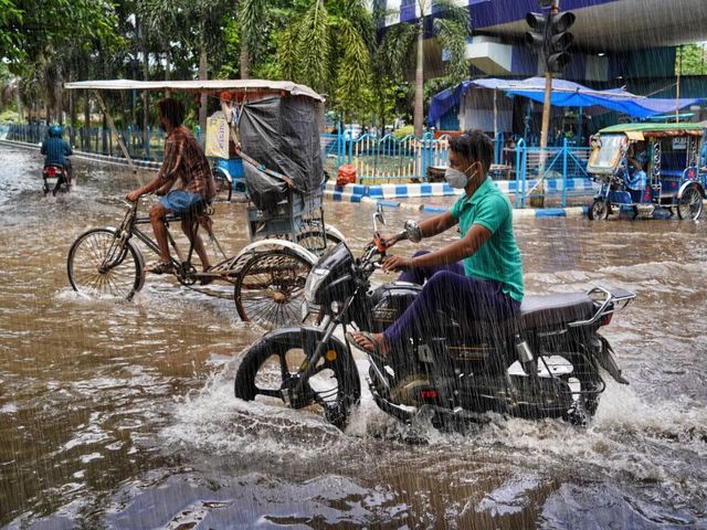 Rikschas und ein Motorrad auf einer überfluteten Straße in Kalkutta
