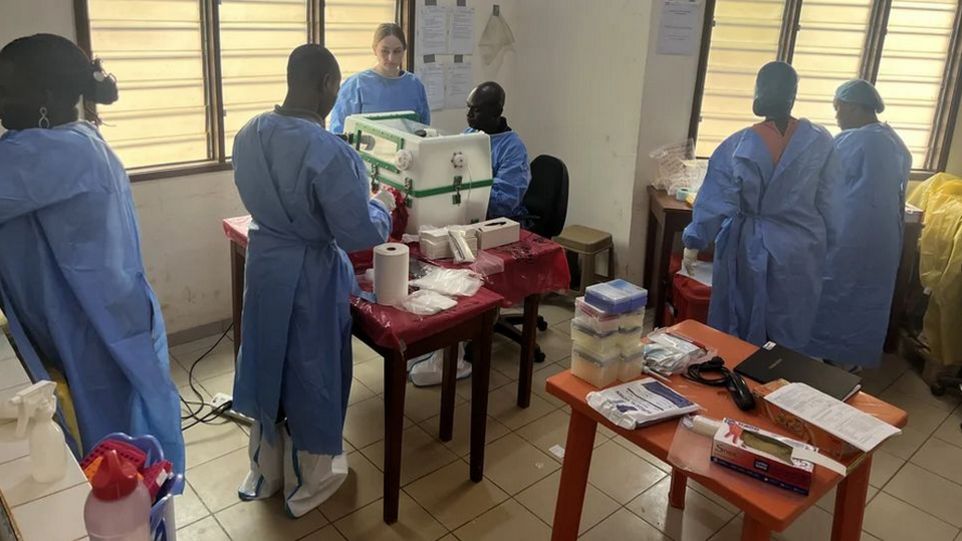 Laborschulung zur Diagnose von MPOX im Labor für hämorrhagisches Fieber in Conakry, Guinea Foto von medizinischen Fachkräften in blauer Schutzkleidung, die in einem Laborraum an verschiedenen medizinischen Geräten arbeiten