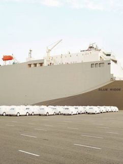 Ein riesiges Frachtschiff mit der Aufschrift "Blue Ridge Highway" und viele weiße Autos im Hafengelände.
