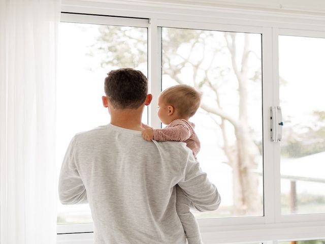 Vater mit Kleinkind auf dem Arm, aus dem Fenster schauend