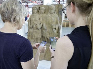 Zwei Frauen mit Handy vor Museumsrelief