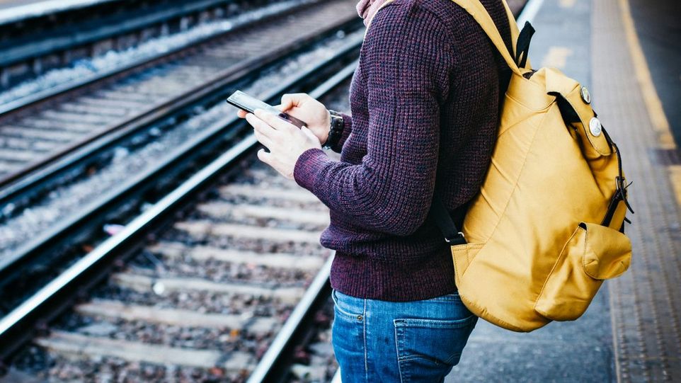 Die neue Seasn-App unterstützt junge Menschen bei der Planung ihrer finanziellen Zukunft. Junger Mann mit Smartphone, an einem Bahnhofsgleis stehend