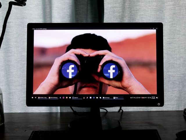 Bildschirm mit Foto eines Mannes, der durch ein Fernrohr schaut, dessen Linsen das Facebook-Logo zeigen