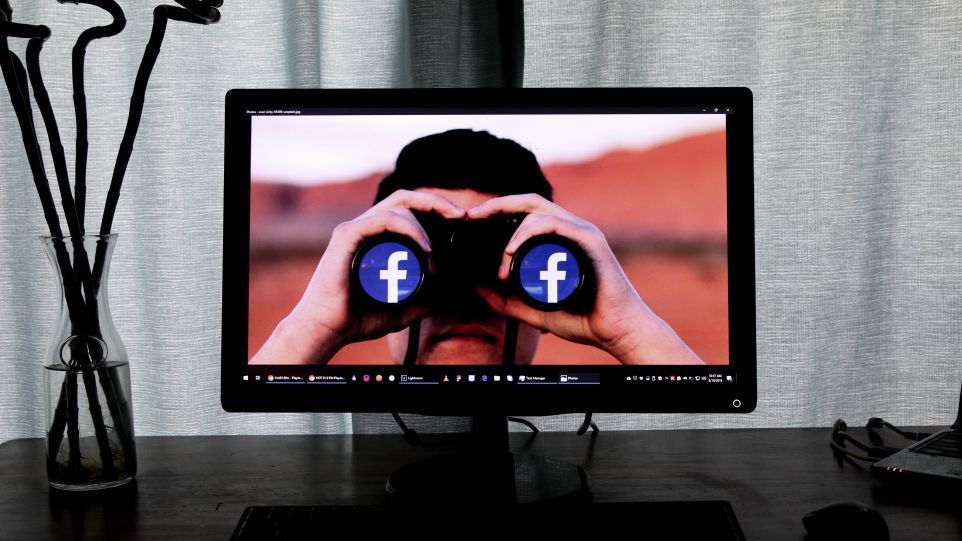 Bildschirm mit Foto eines Mannes, der durch ein Fernrohr schaut, dessen Linsen das Facebook-Logo zeigen