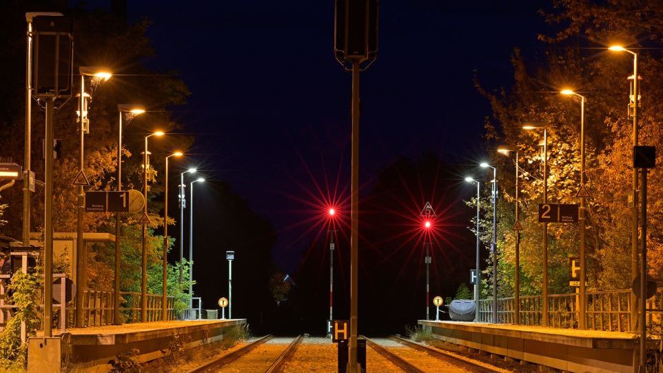 An sechs ländlichen Bahnhöfen im Westhavelland untersuchten Forschende die Anziehungskraft verschiedener Leuchten auf fliegende Insekten. Nächtlicher Bahnhof mit beleuchteten Gleisen und roten Signalen