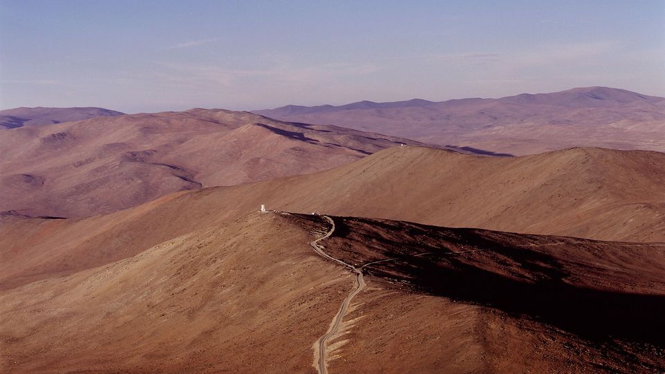 Zielort Paranal, Heimat des VISTA-Teleskops. Kahle Berglandschaft mit einem Weg, der auf ein Gebäude in der Ferne zuläuft