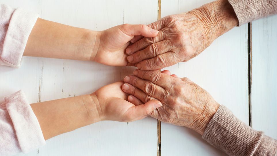 Zwei Hände einer jüngeren Person umfassen die Hände einer älteren Person