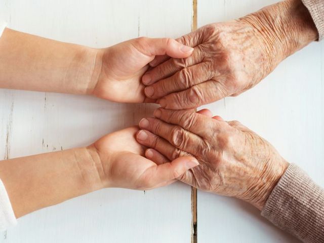 Zwei Hände einer jüngeren Person umfassen die Hände einer älteren Person