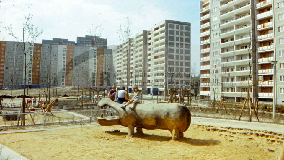 Ein Spielplatz mit Kindern auf einem Holzflusspferd, umringt von Plattenbauten