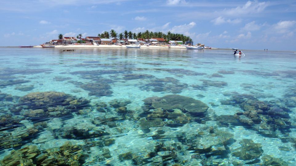 Flache Koralleninseln wie diese Insel im indonesischen Spermonde Archipel sind Gefährdungen durch Meeresspiegelanstieg und andere Umweltveränderungen besonders ausgesetzt. Mit flachen Häuseren dicht besiedelte Koralleninsel, umgeben von türkisem Meer.