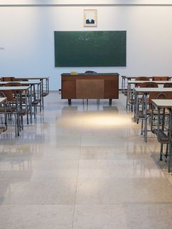 Tische und Stühle vor einer Tafel in einem leeren Klassenraum